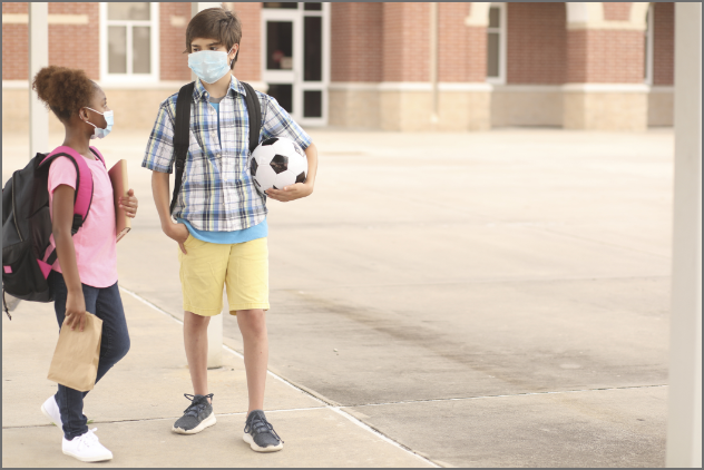 Two children talking with masks on and holding a soccer ball